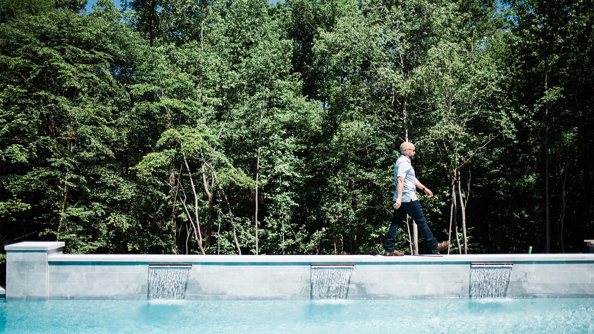 Wide shot of Chris Jones walking alongside concrete pool, featuring waterfalls in North Carolina