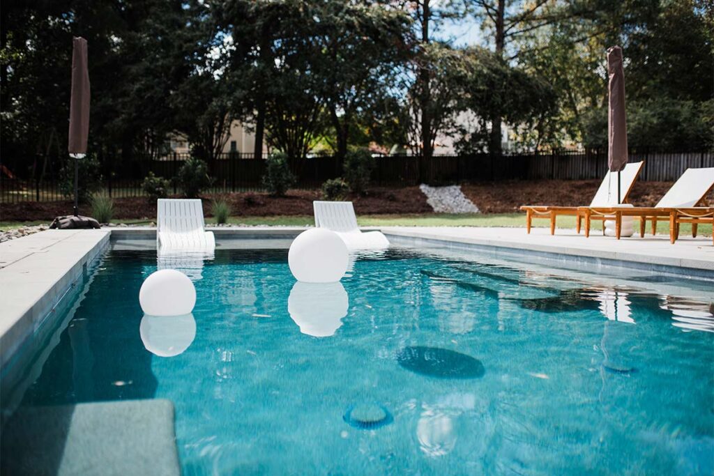 Side view of concrete cray pool with pool chairs and floating spheres