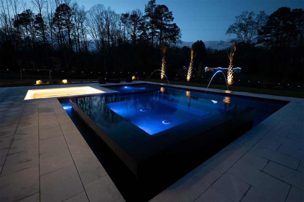 Wide shot of Modern Apex at night showcasing pool lighting, outdoor lighting, and black mirror spa
