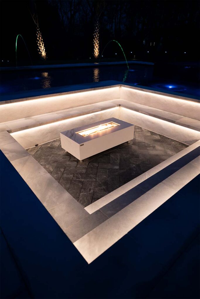 Modern Apex concrete pool at night with sunken fire pit lounge in focus, through use of outdoor lighting and active fire pit